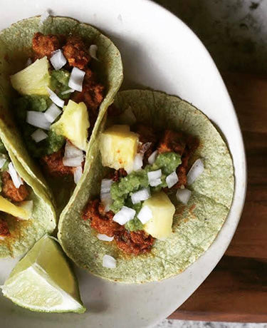 Plate with three tacos made with green tortillas.