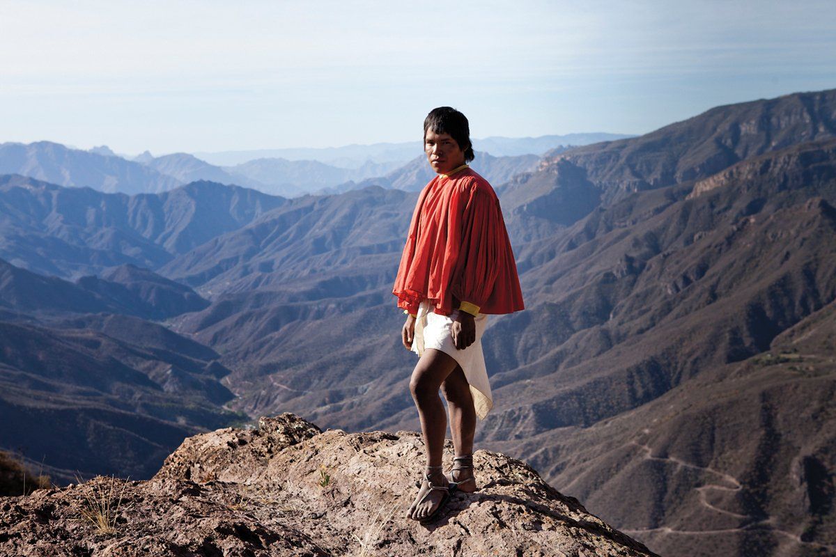 Tarahumara woman standing on a mountain with a mountain range in the background.
