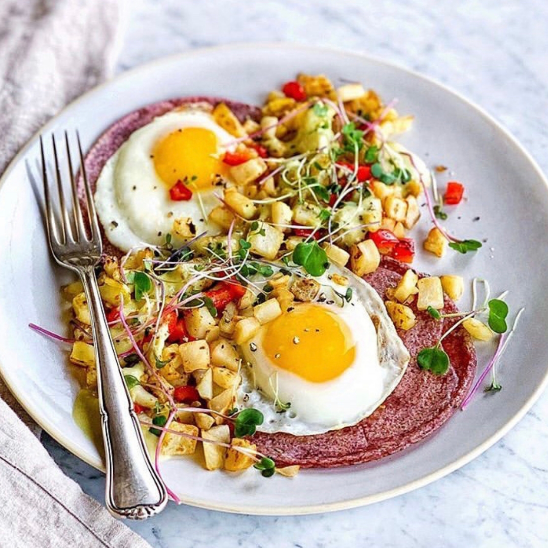 A plate with a breakfast of eggs, peppers, potatoes, and pink corn tortillas.