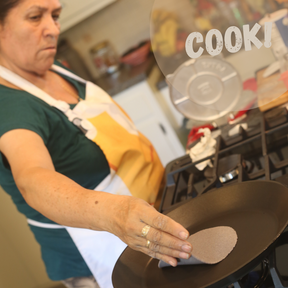 Woman placing raw tortilla on a pan with the text "cook"
